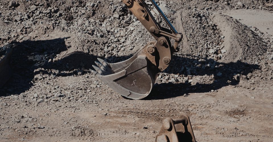 Excavator bucket digging into soil at a construction site, representing site investigation and ground disturbance